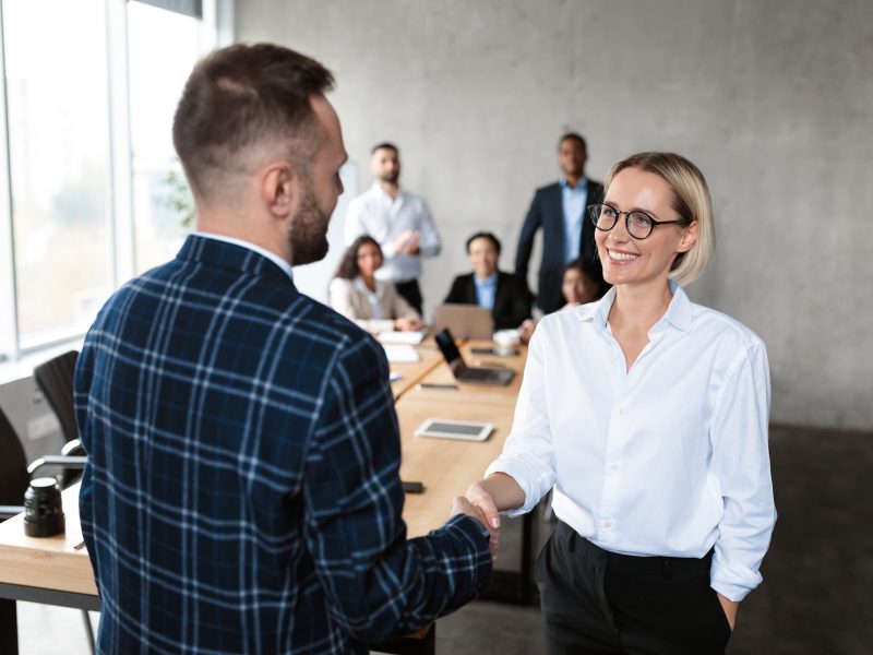 Business Career Promotion. Businessman Shaking Hands With Happy Businesswoman Employee After Successful Deal During Corporate Meeting In Office. Business People Handshaking. Partnership And Agreement